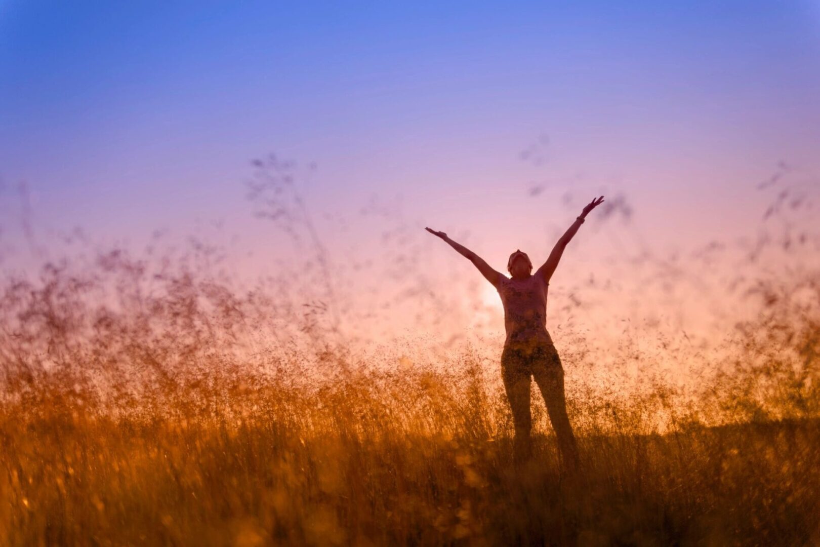 A woman standing in the grass with her arms outstretched.