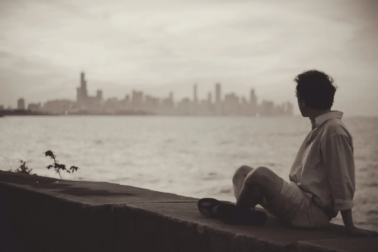 A person sitting on the side of a body of water.