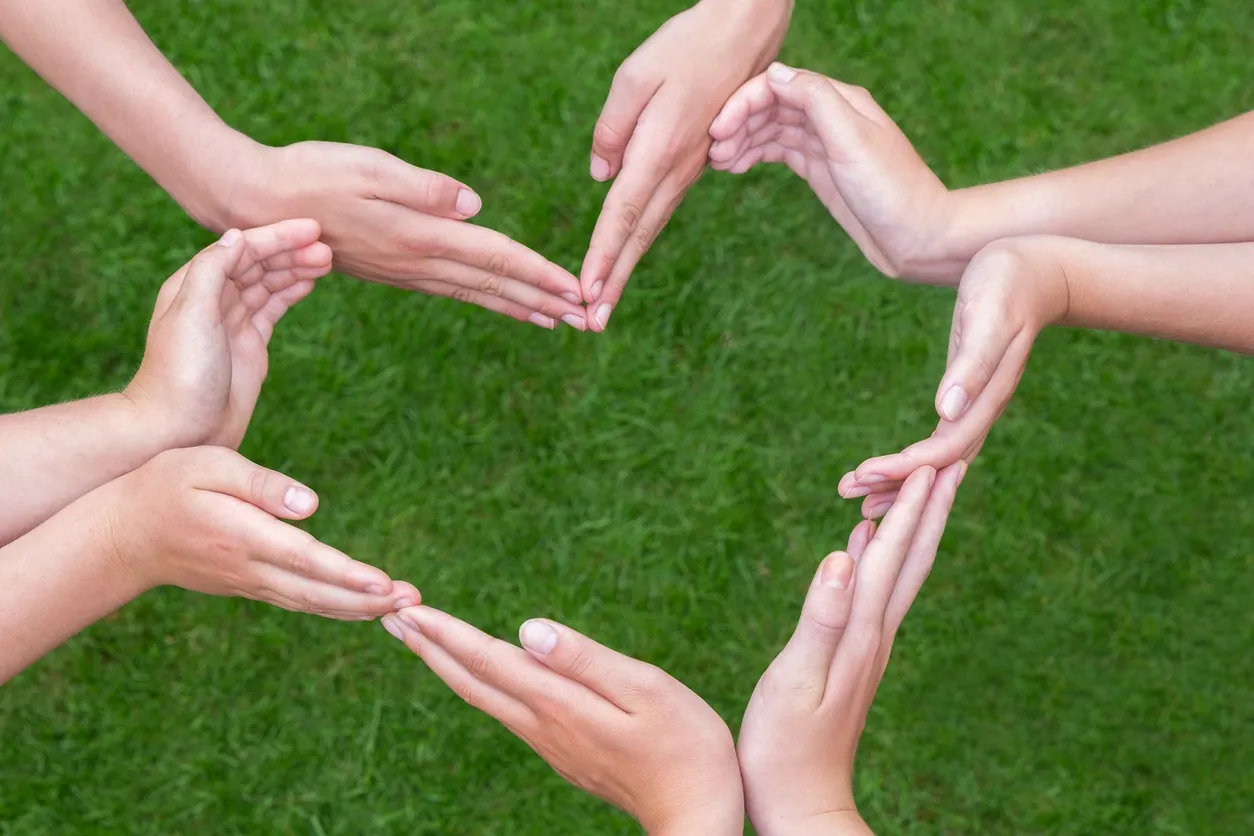 A group of hands are forming the shape of a heart.